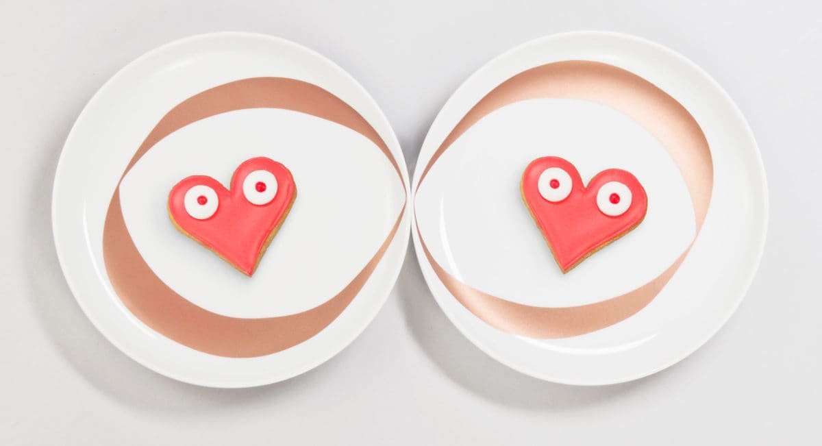 Assiettes infini : Chaque assiette blanche est ornée d'un anneaux cuivré. Mises côte à côte, cela donne un dessin de Ruban de Moebuis. Symbole de l'amour à l'infini. Ici, sont posés sur les assiettes deux gâteaux rouges en forme de coeur, réalisés par la pâtisserie Bogato. Assiettes créees pour le DesignerBox 21 par Ich&Kar