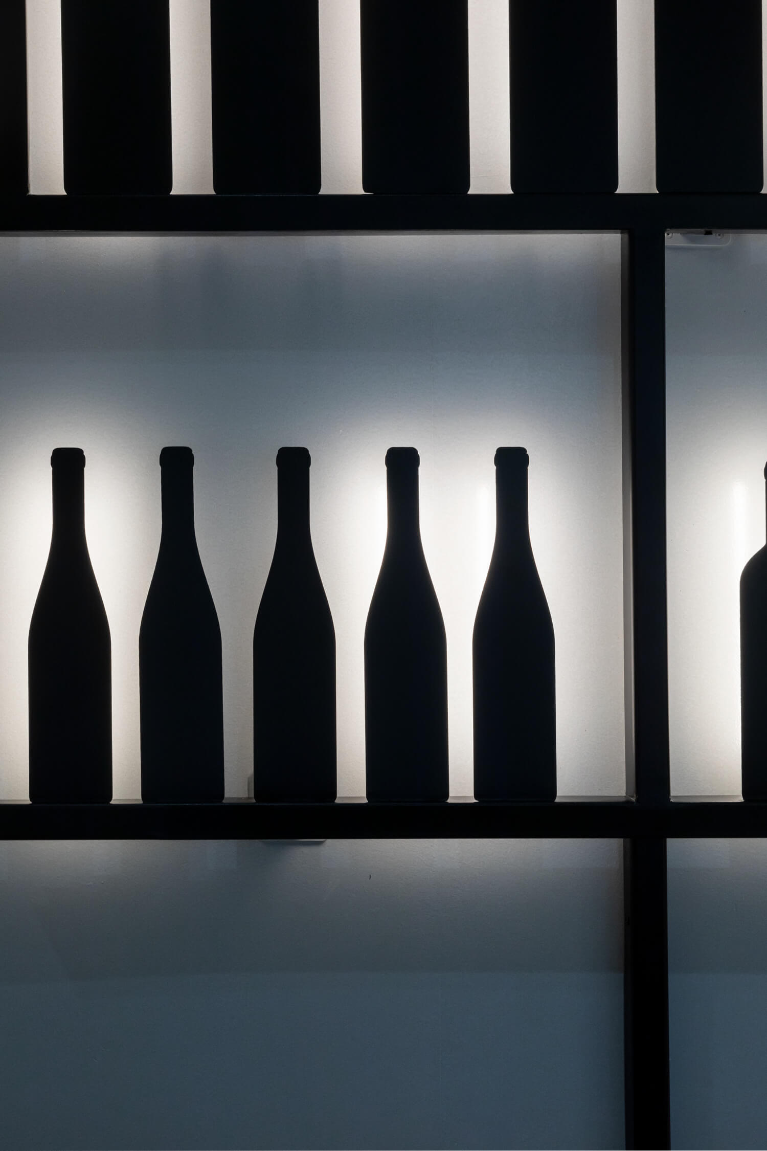 Zoom sur le mur dessiné par IchetKar, bouteilles et étagères en metal noir, rétro éclairées façon ombre chinoise